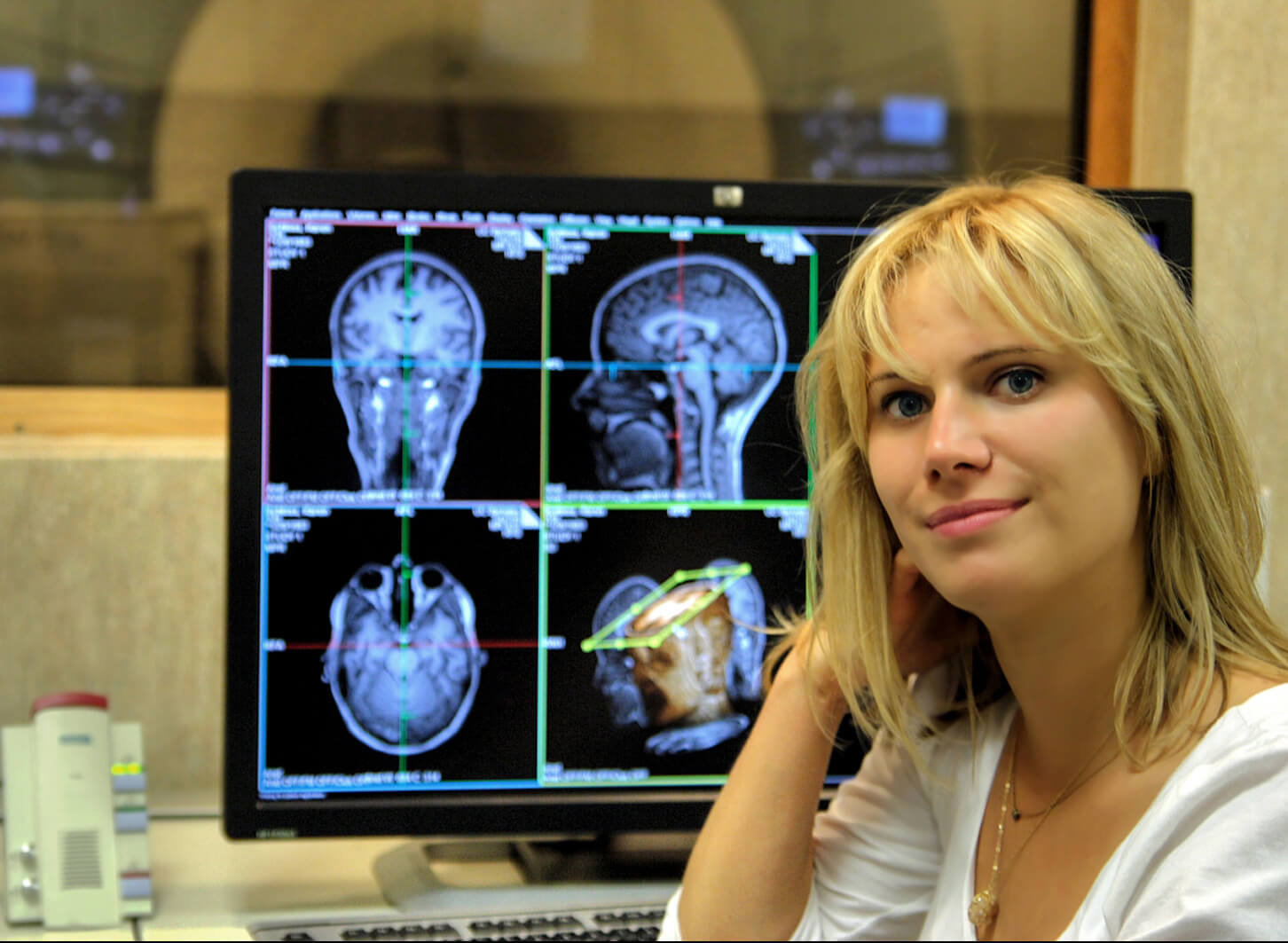 Emily Jacobs sitting in front of a computer monitor with black and white images of human brain scans.